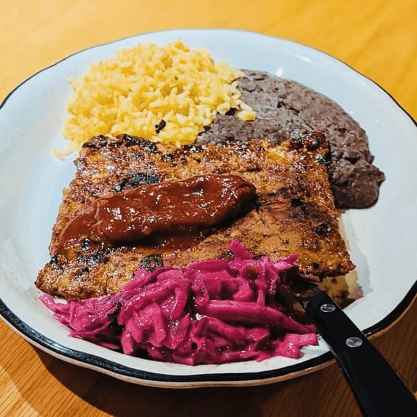 Grilled steak with red sauce, yellow rice, black beans, and pickled red cabbage on a white plate.