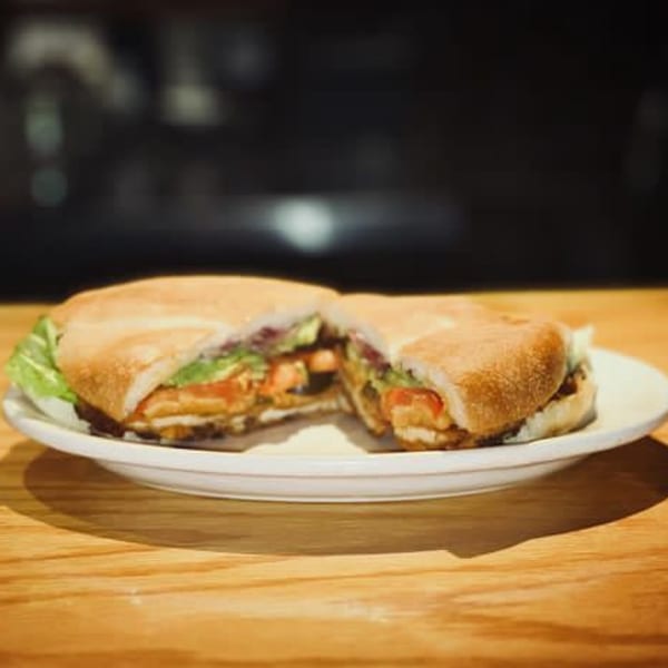 A Mexican torta sandwich, cut in half, with lettuce, tomato, and meat on a white plate.