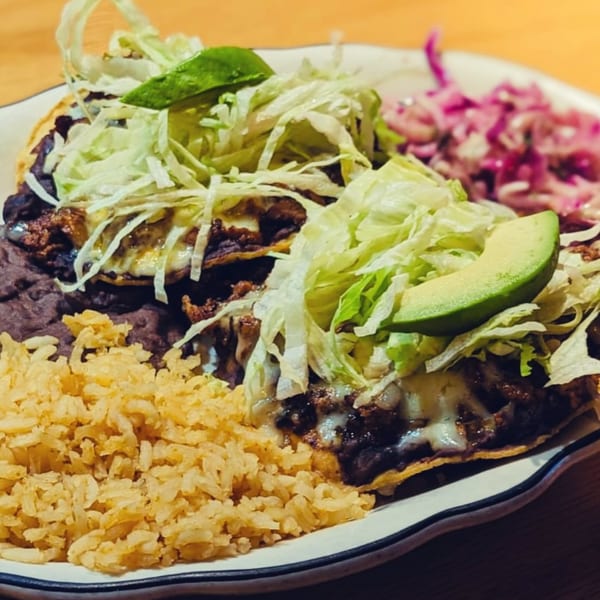 Mexican tostadas with black beans, melted cheese, shredded lettuce, avocado, rice, and pickled onions.