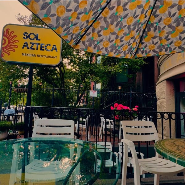 Sol Azteca Mexican Restaurant sign above an outdoor patio with tables, chairs, and a patterned umbrella.
