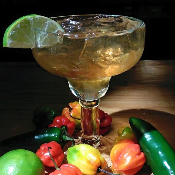 A margarita with a lime wedge, surrounded by colorful habanero and jalapeño peppers.