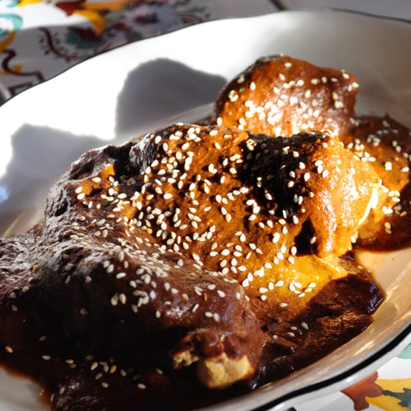 Chicken mole with rich brown sauce and sesame seeds on a white plate at Sol Azteca.