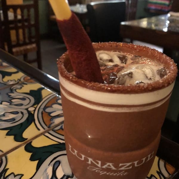 A Sol Azteca Michelada in a branded clay cup with a chili-dusted straw on a tiled counter.