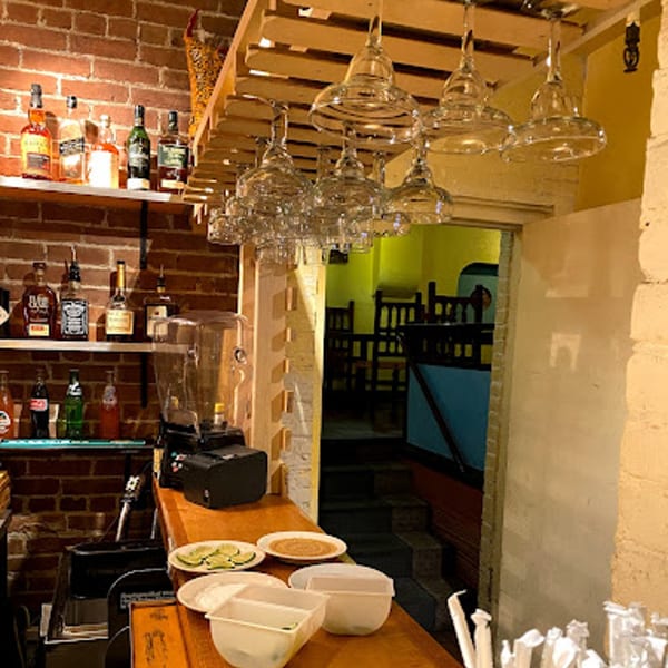 A bar area with liquor bottles, margarita glasses, and a view into a dining room.
