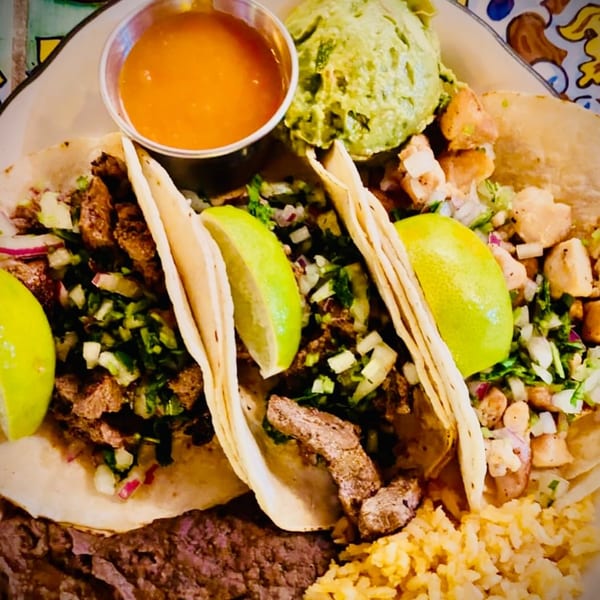 Three Sol Azteca tacos with meat, cilantro, onions, lime, guacamole, rice, and beans.